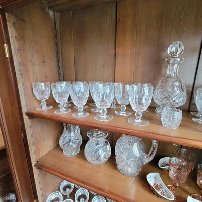 Collection of vintage cut glass and crystal stemware, pitchers, and a decanter displayed on wooden cabinet shelves.