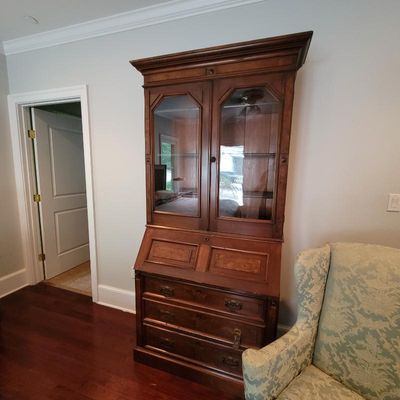 Antique wooden secretary desk with a glass-front upper hutch, drop-front writing surface, and three lower drawers.
