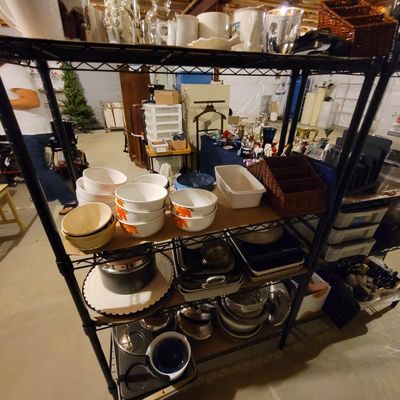 Black wire shelving unit filled with kitchenware, including ceramic mixing bowls with autumn leaf patterns, baking dishes, and stainless...