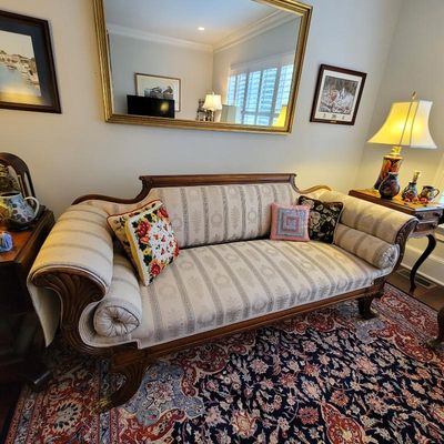 Empire-style mahogany sofa featuring striped damask upholstery, carved scroll arms, and matching bolster pillows, displayed on an...