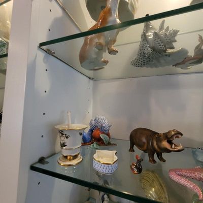 Collection of porcelain and ceramic animal figurines, including a Herend blue fishnet squirrel and a brown hippopotamus, displayed on...