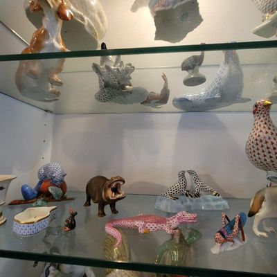Collection of Herend porcelain animal figurines, featuring fishnet patterns in various colors, displayed on glass shelves.