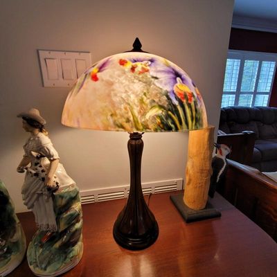 Reverse-painted glass table lamp featuring a floral motif with purple irises, set on a dark metal base.