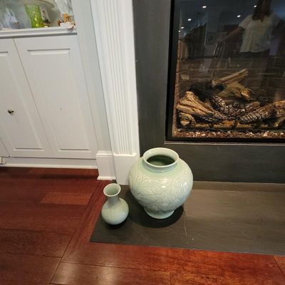 Two pale green celadon-style ceramic vases, including a large round vessel with carved floral motifs and a smaller bottle-shaped vase,...