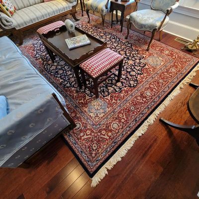 Large Persian-style area rug featuring an intricate floral design in red, navy blue, and cream tones with fringed edges.