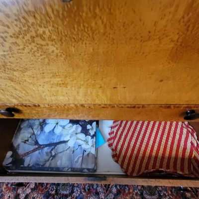 Vintage birdseye maple dresser drawer, partially open to reveal stored linens and a floral-patterned box.