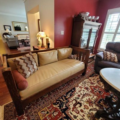 Mission-style oak daybed with tan vinyl cushions, shown alongside a traditional patterned area rug and a dark wood china cabinet.