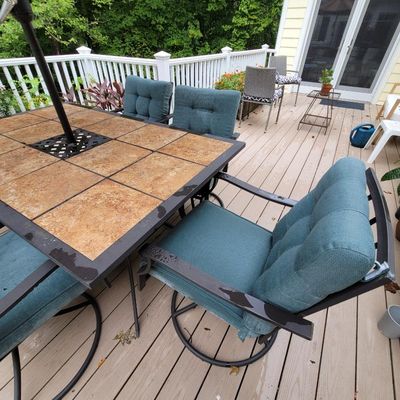 Outdoor dining set featuring a tile-top table with a metal frame and matching swivel chairs with teal cushions.