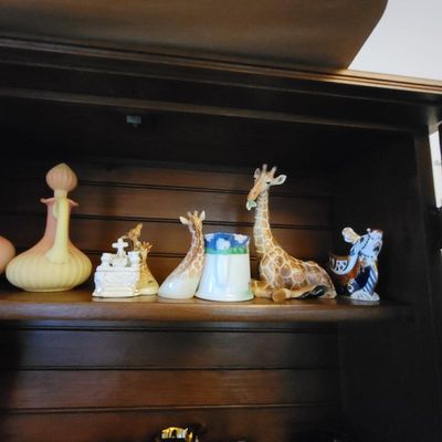 Collection of vintage ceramic and glass figurines, including several giraffe figures, a small white church, and a yellow satin glass...