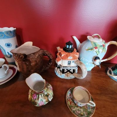 Collection of decorative ceramic teapots and pitchers, including a lighthouse-shaped teapot, a winter bird teapot, and an owl-shaped...