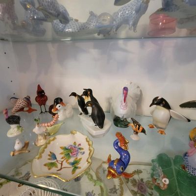 Collection of vintage porcelain and ceramic animal figurines, including penguins, birds, and a turkey, displayed on a glass shelf.