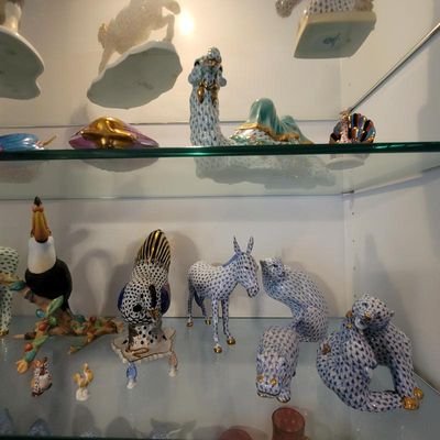 Collection of Herend porcelain animal figurines, featuring their signature fishnet pattern and gold accents, displayed on glass shelves.