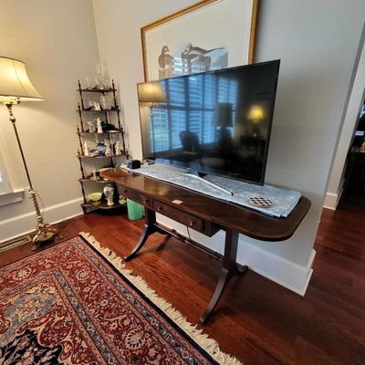 Traditional mahogany sofa table with a curved stretcher base and drawers, supporting a flat-screen television.