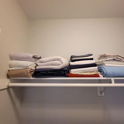 Assorted bed linens, sheets, and blankets neatly folded on a closet shelf.