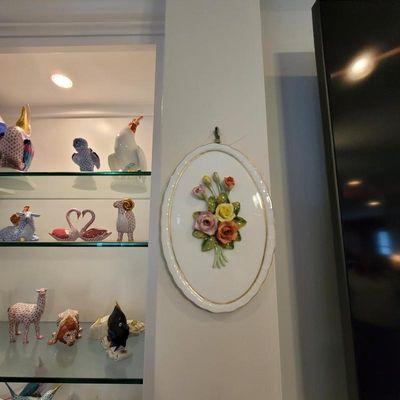 Vintage oval porcelain wall plaque featuring a three-dimensional floral bouquet with gold-trimmed edges, displayed alongside a collection...