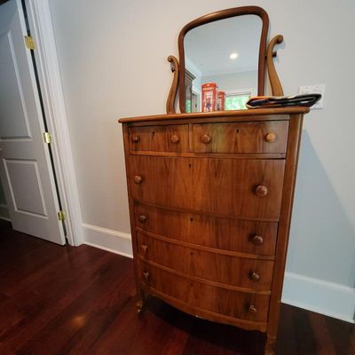 Antique Empire-style cherry wood tall chest of drawers with a matching swivel mirror, featuring a bow-front design and wooden knobs.