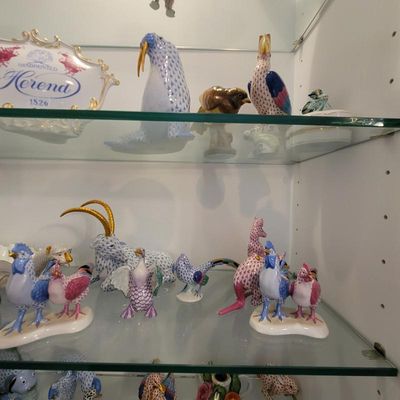 Collection of Herend hand-painted porcelain animal figurines, featuring their signature fishnet pattern, displayed on glass shelves.