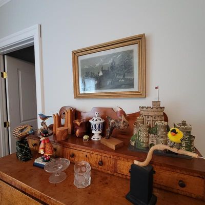 Assorted decorative items displayed on a vintage wooden dresser, including bird figurines, a miniature castle model, glassware, and a...