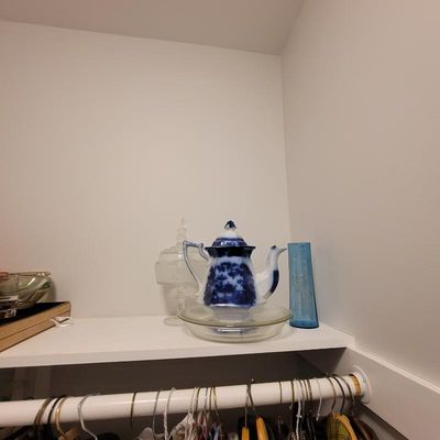 Flow blue porcelain teapot with a matching lid, displayed on a closet shelf alongside a clear glass lidded jar and a blue glass vase.
