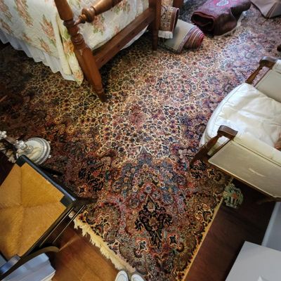 Large Persian-style area rug featuring an intricate floral medallion pattern in red, blue, and cream tones, shown in a bedroom setting.