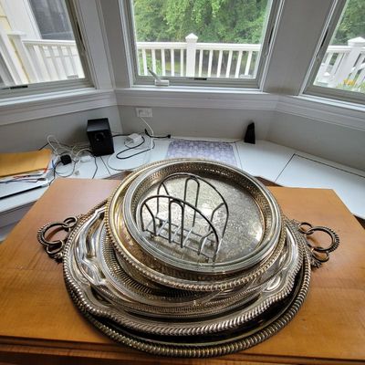 Stack of vintage silver-plated serving trays in various sizes and designs, topped with a wire toast rack.