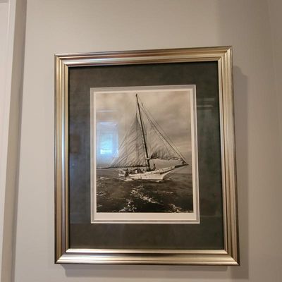 Framed black and white photograph of a sailboat at sea, presented in a silver-toned frame with a dark green mat.