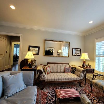 Traditional living room furniture including a striped camelback sofa with carved wood trim, flanked by matching end tables with lamps,...