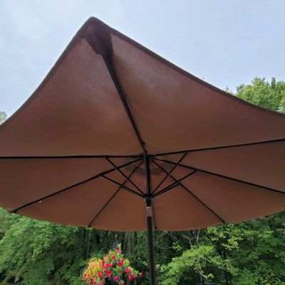 Large brown outdoor patio umbrella with a black metal frame, shown open against a backdrop of trees.