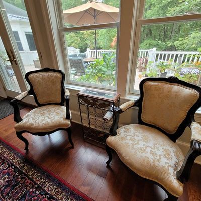 Pair of French Provincial style armchairs with dark wood frames and cream and gold damask upholstery, flanking a metal wine rack side table.