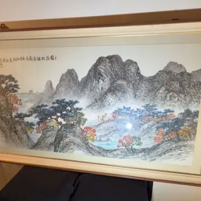 Large framed Chinese landscape painting on paper, depicting misty mountains, pine trees, and a river, housed in a wooden frame with a...