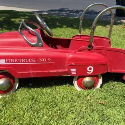 Vintage Murray Fire Truck No. 9 pedal car, featuring a red metal body, chrome steering wheel and grab bars, and a front-mounted bell.