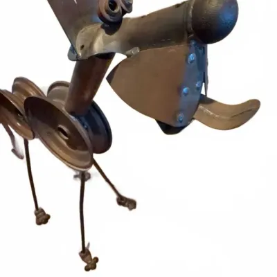 Whimsical scrap metal dog sculpture, crafted from repurposed industrial parts including pulleys, bolts, and sheet metal.