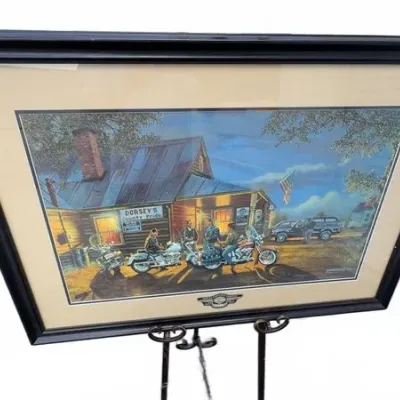 Framed Harley-Davidson art print depicting motorcycles parked outside a rustic general store, double-matted in a black wooden frame.