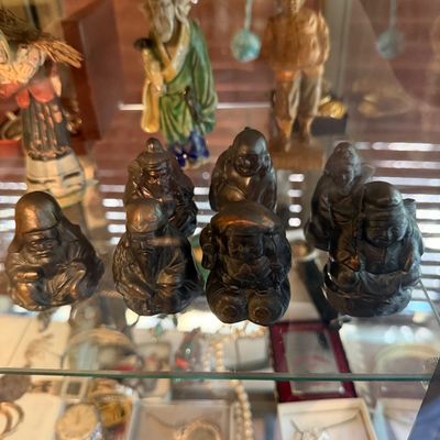 Collection of small Asian figurines, including dark metal or resin Seven Lucky Gods figures and glazed ceramic statues, displayed on a...