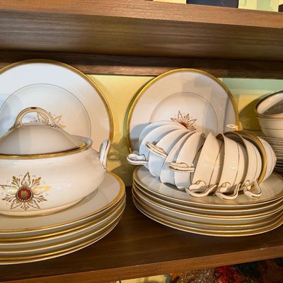Sale Photo Thumbnail #131: Vintage Lenox fine porcelain dinnerware service featuring gold trim and a central crest emblem, including a covered tureen, stacked plates, and teacups.