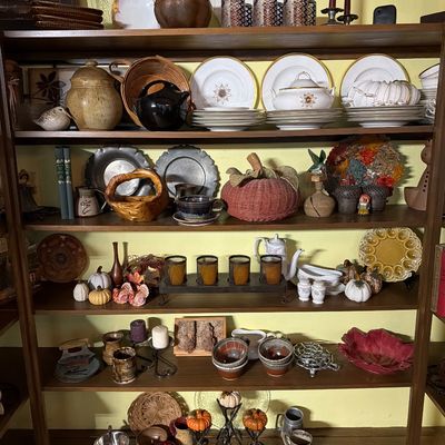 Wooden bookshelf filled with an assortment of vintage tableware, pottery, decorative pumpkins, and rustic home decor.