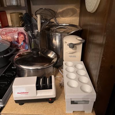 Sale Photo Thumbnail #148: Assorted kitchen appliances and cookware, including a Chef's Choice electric knife sharpener, a Black & Decker electric can opener, stainless steel stockpots, and a white plastic egg holder.