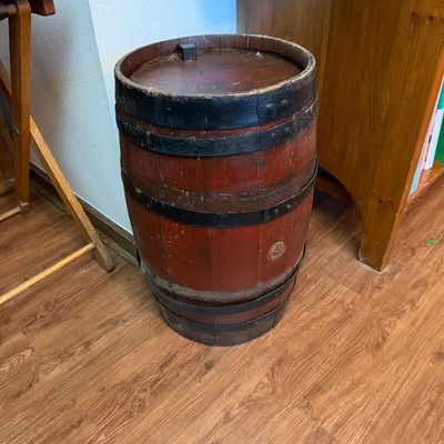 Vintage wooden barrel with a reddish-brown finish and black metal bands, showing some wear and age.