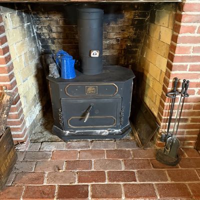 Vintage Earth Stove wood-burning fireplace insert with gold-tone trim, set inside a brick hearth alongside fireplace tools and blue...