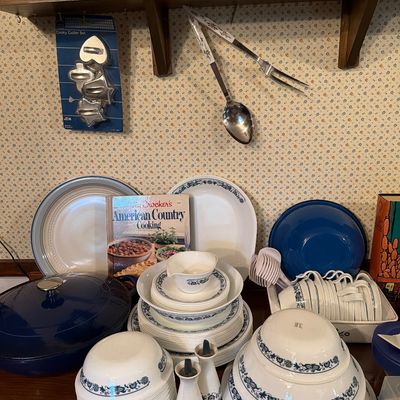Sale Photo Thumbnail #140: Vintage Corelle Old Town Blue dinnerware set, including plates, bowls, cups, and matching salt and pepper shakers, displayed alongside a blue enameled cast iron Dutch oven and a Betty Crocker cookbook.