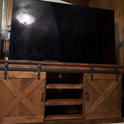 Sale Photo Thumbnail #134: Rustic wooden media console featuring sliding barn-style doors with black metal hardware and open center shelving, shown with a large flat-screen television.