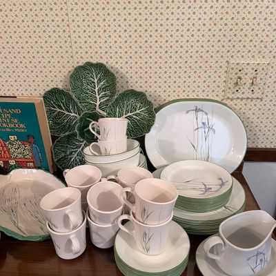 Vintage ceramic dinnerware set featuring a delicate purple iris and green grass motif, accompanied by a green cabbage leaf serving platter.