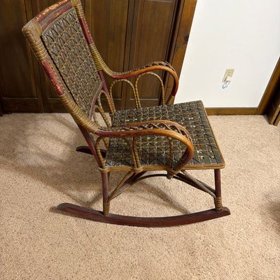 Vintage wicker and wood rocking chair featuring a woven back and seat with green and natural tones, showing some wear on the wooden frame.