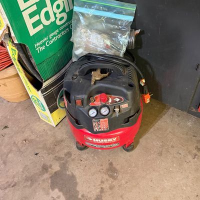 Sale Photo Thumbnail #274: Husky portable pancake air compressor with attached wheels, telescoping handle, and extra accessories in a plastic bag.