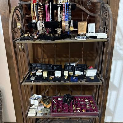 Sale Photo Thumbnail #161: Vintage costume jewelry collection, including beaded necklaces, watches, and boxed pins, displayed on a four-tier wrought iron baker's rack.