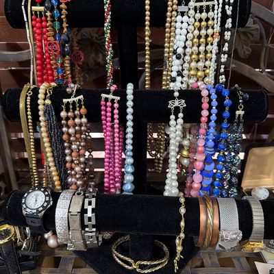 Sale Photo Thumbnail #166: Assortment of vintage costume jewelry, including multi-strand beaded necklaces, faux pearls, and various metal and mesh bracelets, displayed on a black velvet T-bar stand.