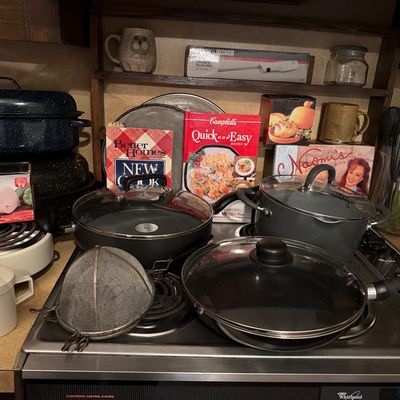 Sale Photo Thumbnail #147: Assorted kitchenware including non-stick pots and pans with glass lids, a blue speckled roasting pan, cookbooks, and various kitchen utensils.