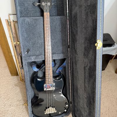 Black Epiphone EB-0 electric bass guitar with chrome hardware, resting inside its plush-lined hardshell case.