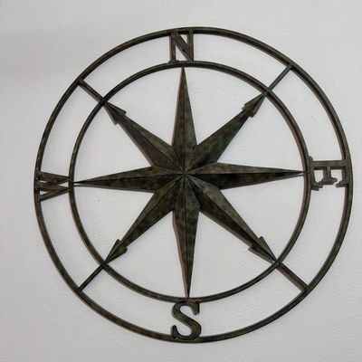 Large metal compass rose wall decor with a distressed, dark bronze finish.