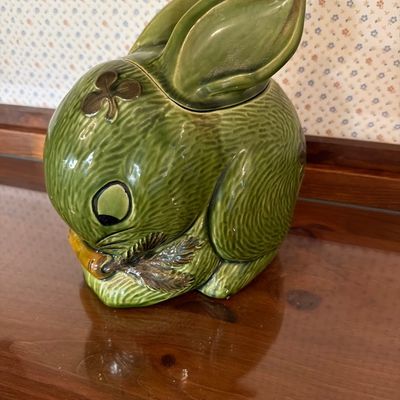 Vintage green ceramic rabbit cookie jar featuring a textured fur pattern, a shamrock detail on its head, and a carrot in its paws.